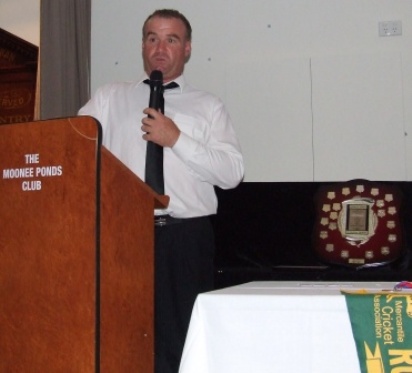 Sean O'Kane takes to the microphone to respond after being awarded the Lindsay Jones. The shield is beside him; above the Fifths runner-up flag.