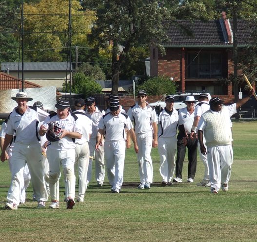 Matchwinning batsman Channa DeSilva waves a stump to the crowd, as the triumphant team comes off with umpire Brian Lazzaro, led by coach Rex Bennett and keeper Peter Golding on the left.